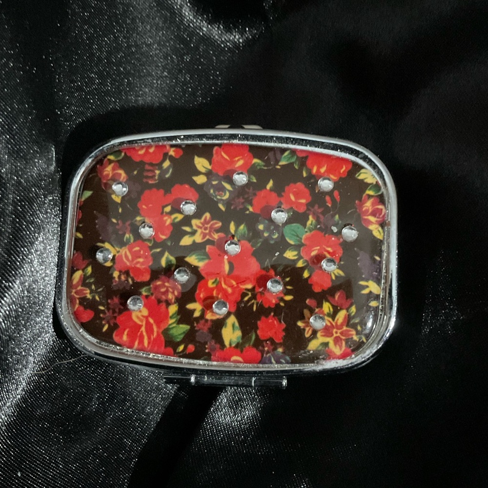 A compact, metal, floral-patterned pill case or travel medicine organizer 2339